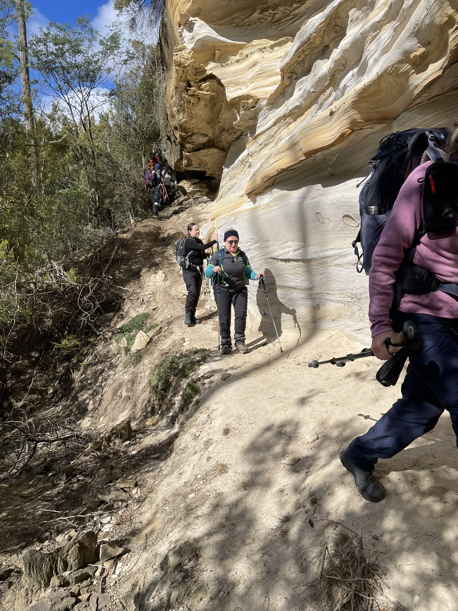 Hikers walking on a narrow path with the sandstone cliffs above and the Bluff River Gorge below path 