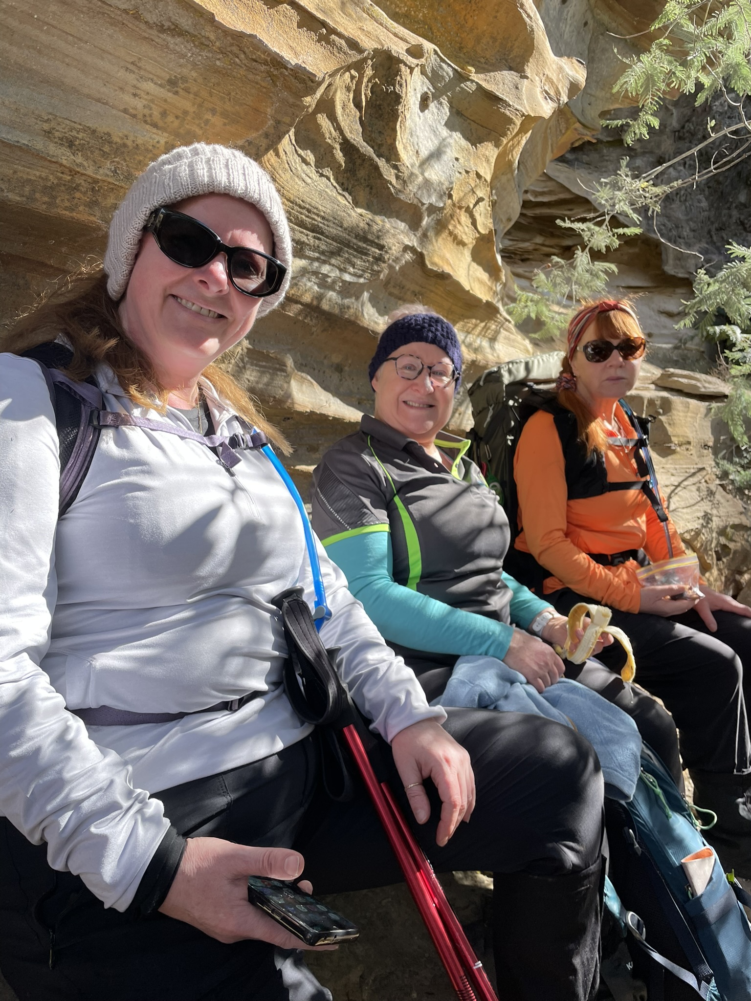 3 hikers taking a break and are seated with backs to the Bluff River Gorge sandstone cave 